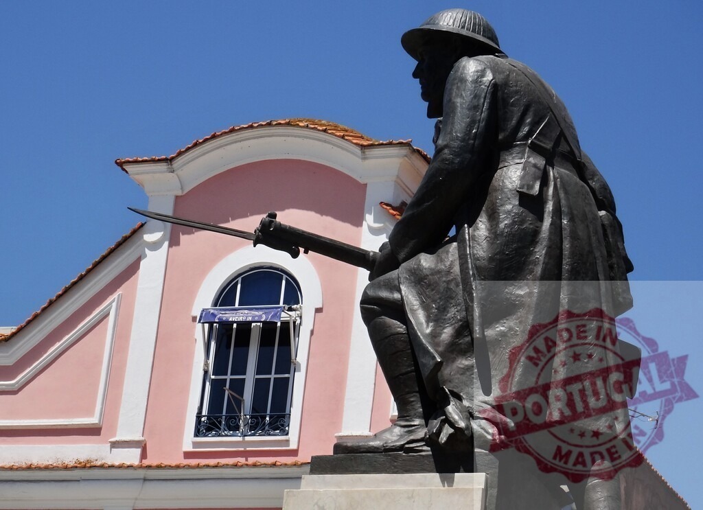 Soldier statue with rifle standing in front of pink building. Aveiro - Portugal | Bronze statue of a soldier with a rifle on a sunny day in Portugal - Realized with Pictrs.com
