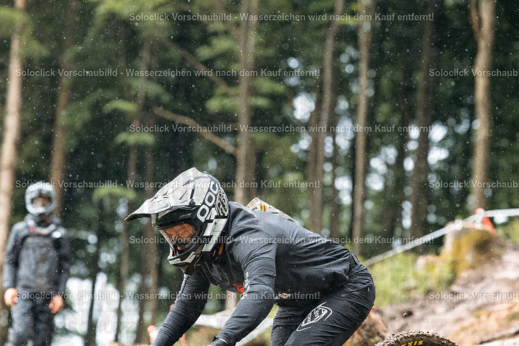 Mountainbiker im Gelände | Das Bild zeigt einen Mountainbiker in voller Montur, der einen steilen, schlammigen Hang hinunterfährt. Der Fahrer ist in voller Aktion und konzentriert sich auf den Weg vor ihm. Der Hintergrund besteht aus dichtem Grün und Bäumen, was die Wildnis der Umgebung betont. - Realisiert mit Pictrs.com
