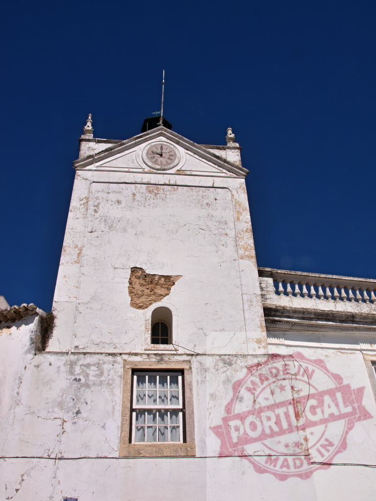 Tavira Portugal clock tower building showing weathered architecture | Weathered white building clock tower standing against a clear blue sky in Tavira, Portugal - Realized with Pictrs.com