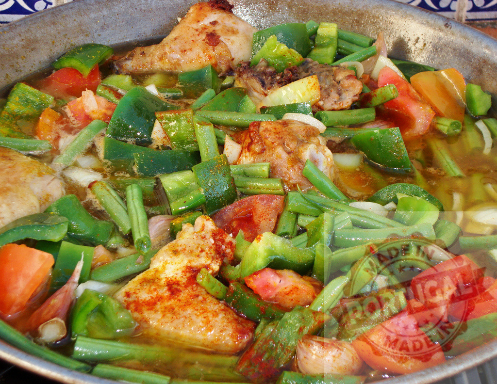 Cooking chicken paella with green beans and bell pepper | Chicken, green beans, bell pepper, and tomatoes simmering in a large pan for paella - Realized with Pictrs.com