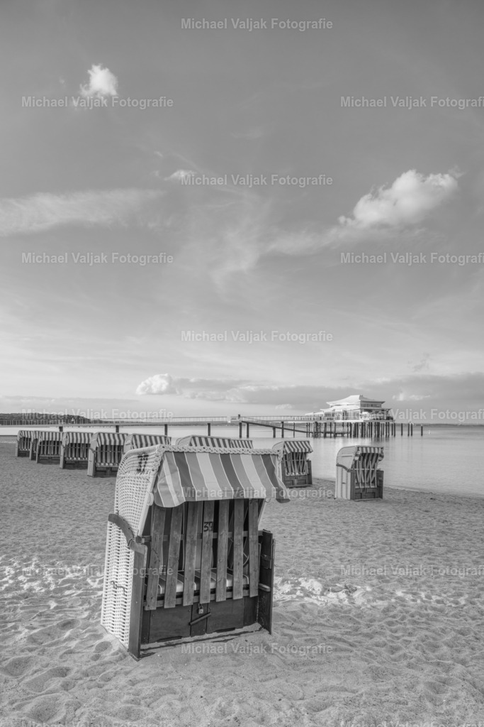 Strandkörbe am Timmendorfer Strand schwarz-weiß | Abends am Timmendorfer Strand, die letzten Sonnenstrahlen des Tages treffen auf die Seebrücke mit dem Teehaus am Ende und ein kleiner Strahl trifft noch auf den Strandkorb im Vordergrund (Schwarz-weiß-Version)  - Realisiert mit Pictrs.com