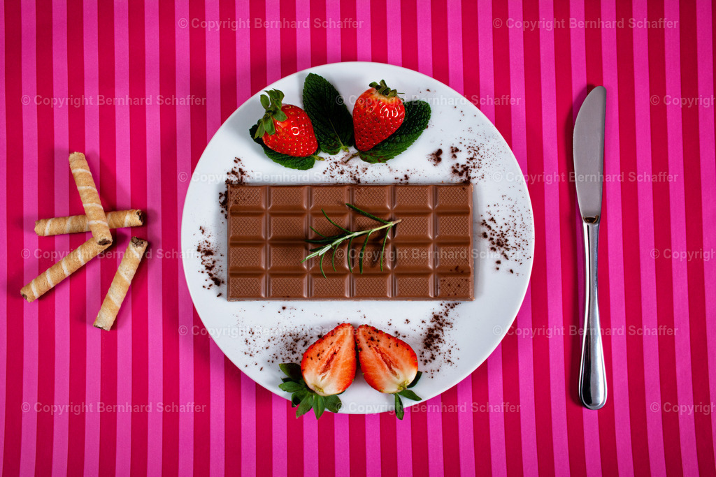 Erdbeer und Schokolade | Eine Tafel Schokolade und Erdbeeren liegen auf einem Teller und daneben Messer und Waffeln. - Realisiert mit Pictrs.com