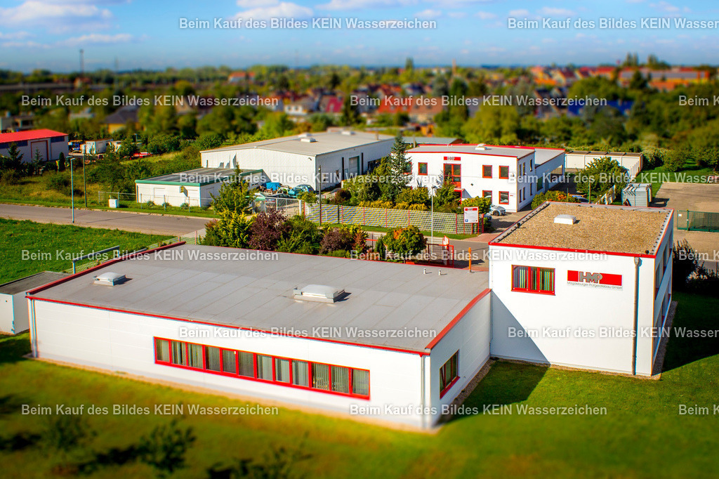 HMP Prüfgerätebau Luftbild-2226-2 | Blick aus der tief fliegenden Drohne auf drei weiße Bürogebäude. Die nahe Perspektive und die klare Architektur der Gebäude werden durch den gezielten Tilt-Shift-Effekt zusätzlich betont.Durch die geringe Schärfezone wirkt der Gebäudekomplex beinahe wie ein Modell oder eine Miniatur. Die ungewöhnliche Bildwirkung lenkt den Blick auf die geometrischen Formen, Fassaden und die Anordnung der drei Gebäude zueinander.Das Motiv zeigt eine weitere Möglichkeit professioneller Unternehmens- und Architekturfotografie: Nicht immer muss ein Standort rein dokumentarisch dargestellt werden. Mit einer gezielt eingesetzten fotografischen Gestaltung kann ein funktionales Büroensemble auch zu einem eigenständigen, aufmerksamkeitsstarken Bild werden.So verbindet die Aufnahme Standortfotografie mit einer bewusst ungewöhnlichen visuellen Bildsprache. - Realisiert mit Pictrs.com