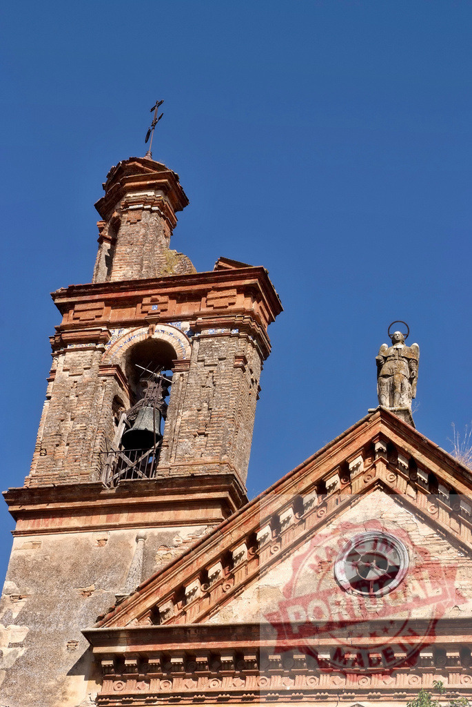 Historic church bell tower and angel statue under blue sky. Spain - Cordoba | Old brick church with a bell, cross, and weathered angel statue on a clear day - Realized with Pictrs.com