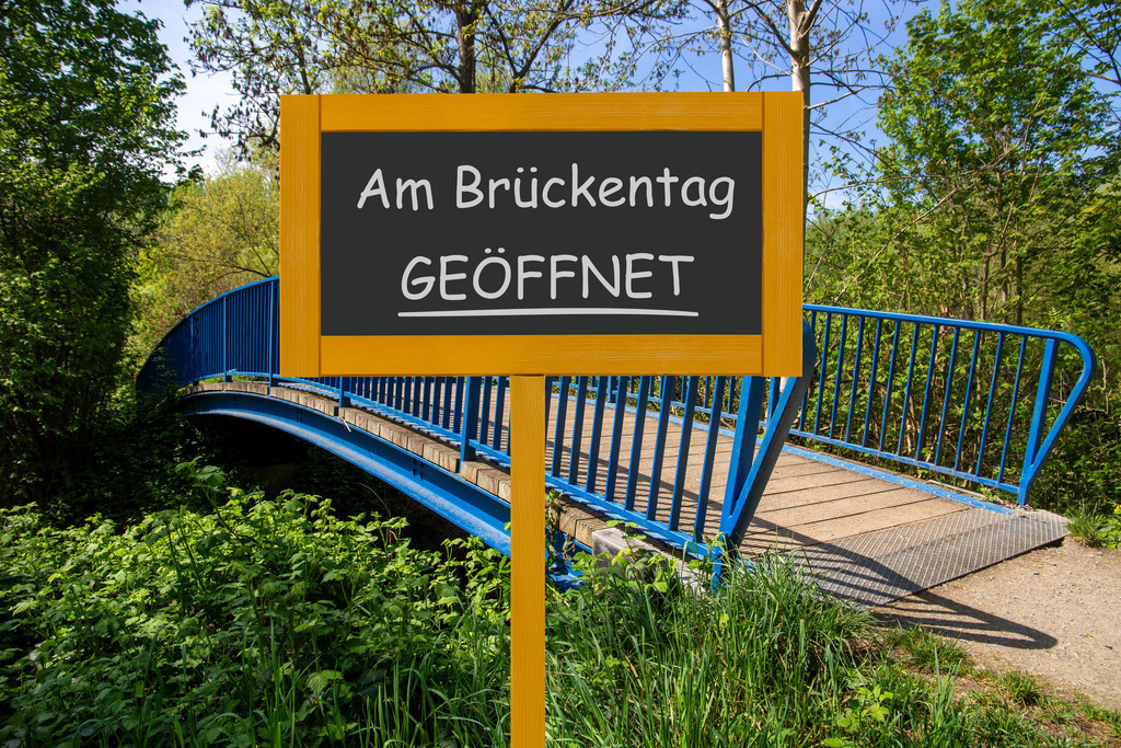 Am Brückentag geöffnet | (Fotomontage) Schild mit der Aufschrift AM BRÜCKENTAG GEÖFFNET vor einer Brücke im Wald - Realisiert mit Pictrs.com