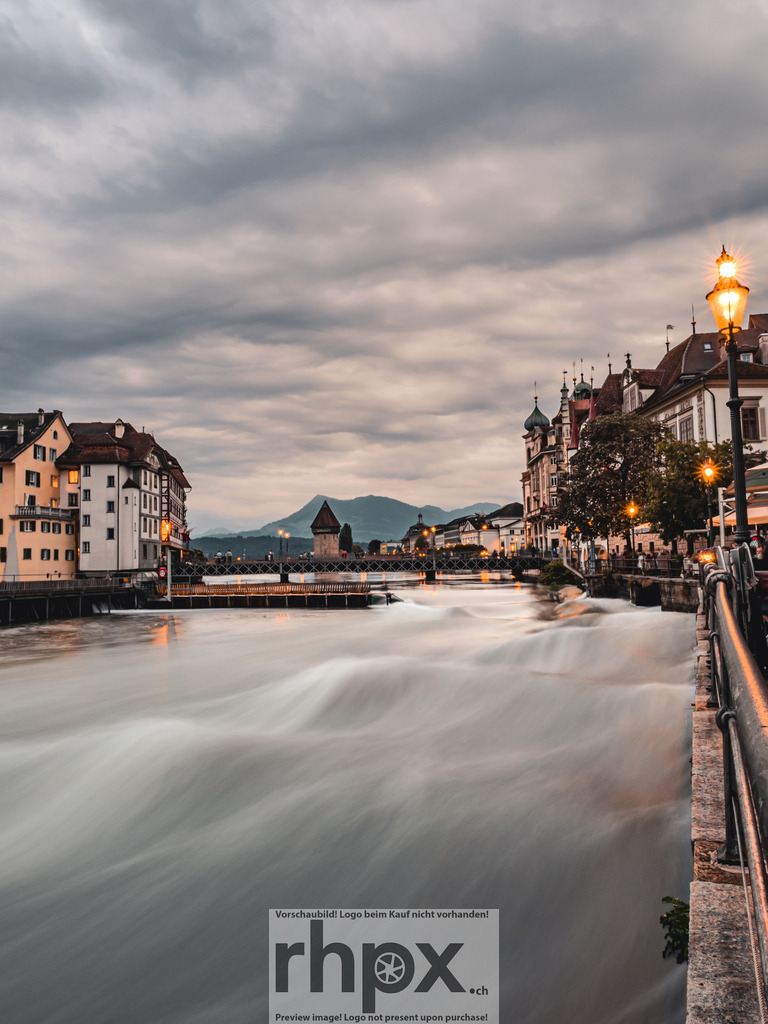 Reuss Luzern – Blick auf die Altstadt | Langzeitaufnahme der Reuss mit Blick auf die Luzerner Altstadt. Die ruhige Wasseroberfläche und das warme Licht der Strassenlaternen zeigen den Übergang vom Tag zur Nacht. - Realisiert mit Pictrs.com
