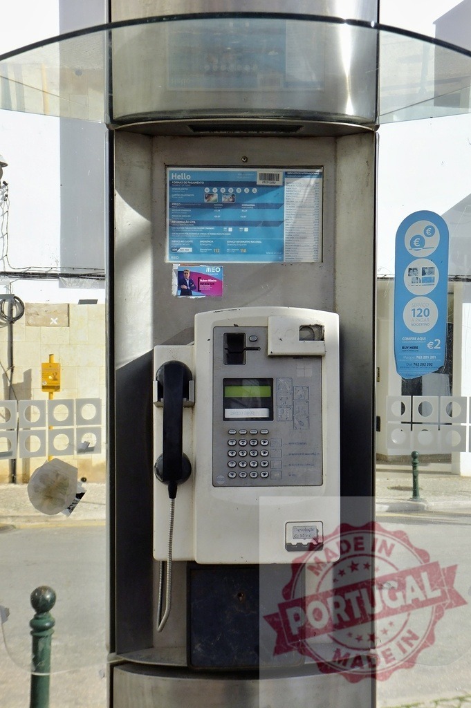 Public telephone inside modern booth standing on a sidewalk | Modern public phone booth with glass protection standing on a sidewalk - Realized with Pictrs.com
