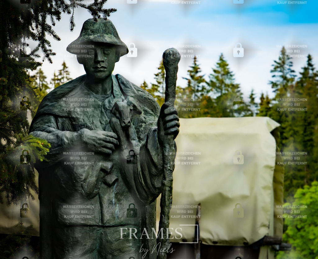 Bauern Statue | Das Foto zeigt eine detailreich aus Stein gehauene Statue, die einen mittelalterlichen Bauern darstellt, der ein Lamm im Arm trägt. Die Figur steht in einem Wald und wird von einem alten, hölzernen Pferdewagen im Hintergrund ergänzt, der der Szene einen historischen und leicht mystischen Charakter verleiht. Die Kombination aus Natur, verwitterter Statue und antikem Wagen schafft eine ruhige, zeitlose Atmosphäre. Die Aufnahme betont die kunstvolle Gestaltung der Steinskulptur, die Struktur des Materials und den Kontrast zwischen der menschlichen Darstellung und der natürlichen Umgebung. - Realisiert mit Pictrs.com