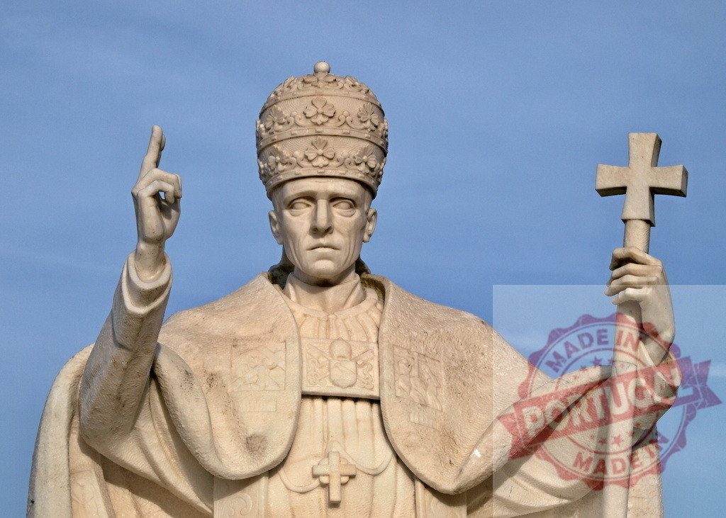 Statue of Pope Pius XI raising his finger and holding a cross | Marble statue of Pope Pius XI holding a cross and raising his right index finger against a blue sky background - Realized with Pictrs.com