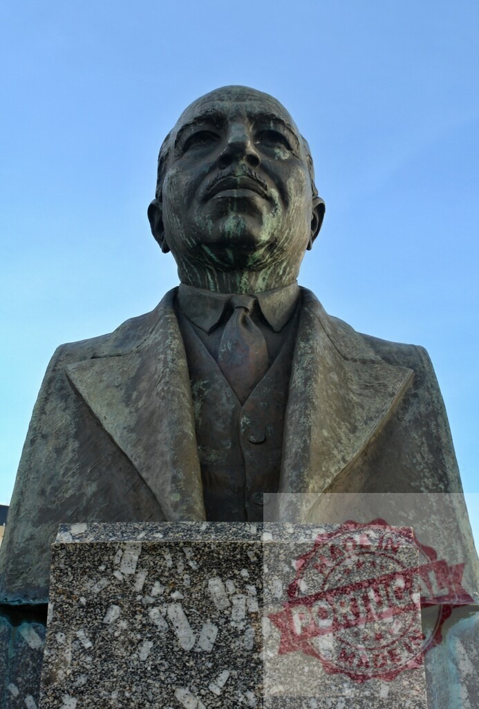 Bronze historical figure bust against clear blue sky | Bronze bust of a historical figure standing on a granite pedestal under a clear sky - Realized with Pictrs.com