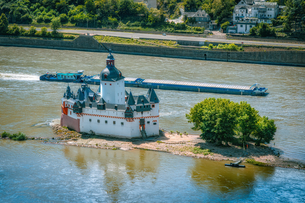 Die Burg Pfalzgrafenstein bei Kaub am Rhein, Schiff fährt vorbei | Die Burg Pfalzgrafenstein (oft auch „die Pfalz“ genannt) ist eine historische Zollburg auf einer Felseninsel im Rhein bei Kaub. Wegen ihrer Form wird sie im Volksmund auch als „das steinerne Schiff“ bezeichnet.Lage &amp; Bau: Sie steht mitten im Strom des Rheins auf der Schieferinsel Falkenau und wurde im Jahr 1326 von Ludwig dem Baier als Zollstelle errichtet.Besonderheit: Die Anlage gehört zu den wenigen Burgen im Mittelrheintal, die im Laufe der Jahrhunderte nie zerstört wurden. - Realisiert mit Pictrs.com