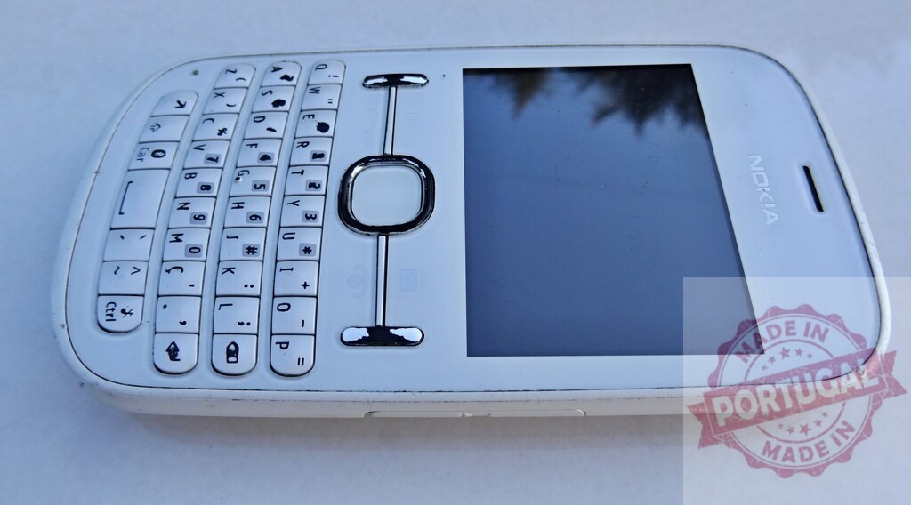 White Nokia Asha 302 mobile phone showing keyboard and screen | White Nokia Asha 302 mobile phone with a QWERTY keyboard and a blank screen resting on a white surface - Realized with Pictrs.com