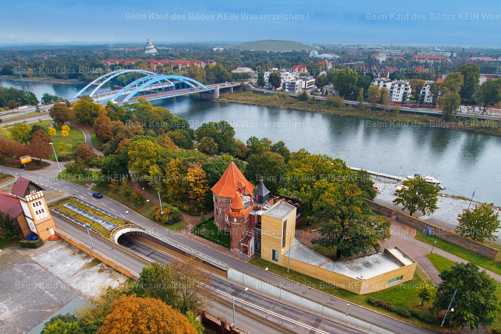 Lukasklause-Otto-von-Guericke-Schleinufer-Magdeburg-5278 | Blick aus der Vogelperspektive auf die Lukasklause am Magdeburger Elbufer. Aus dieser ungewöhnlichen Perspektive zeigt sich das historische Bauwerk von seiner Rückseite mit dem modernen Anbau des Otto-von-Guericke-Zentrums und der darunter verlaufenden Tunneleinfahrt.Die Lukasklause geht auf einen mittelalterlichen Wehrturm aus dem 13. Jahrhundert zurück und war Teil der Magdeburger Stadtbefestigung. Ihren heutigen Namen erhielt die Anlage erst später. Heute erinnert hier das Otto-von-Guericke-Zentrum an den großen Magdeburger Wissenschaftler und Bürgermeister des 17. Jahrhunderts.Besonders interessant ist der Kontrast zwischen dem alten Wehrturm und der modernen Architektur des Erweiterungsbaus. Wo einst die Stadt befestigt und verteidigt wurde, befindet sich heute ein Ort für Wissenschaft, Geschichte und Besucher.Das Luftbild zeigt die Lukasklause einmal aus einer Perspektive, die man vom Boden aus kaum wahrnimmt. - Realisiert mit Pictrs.com