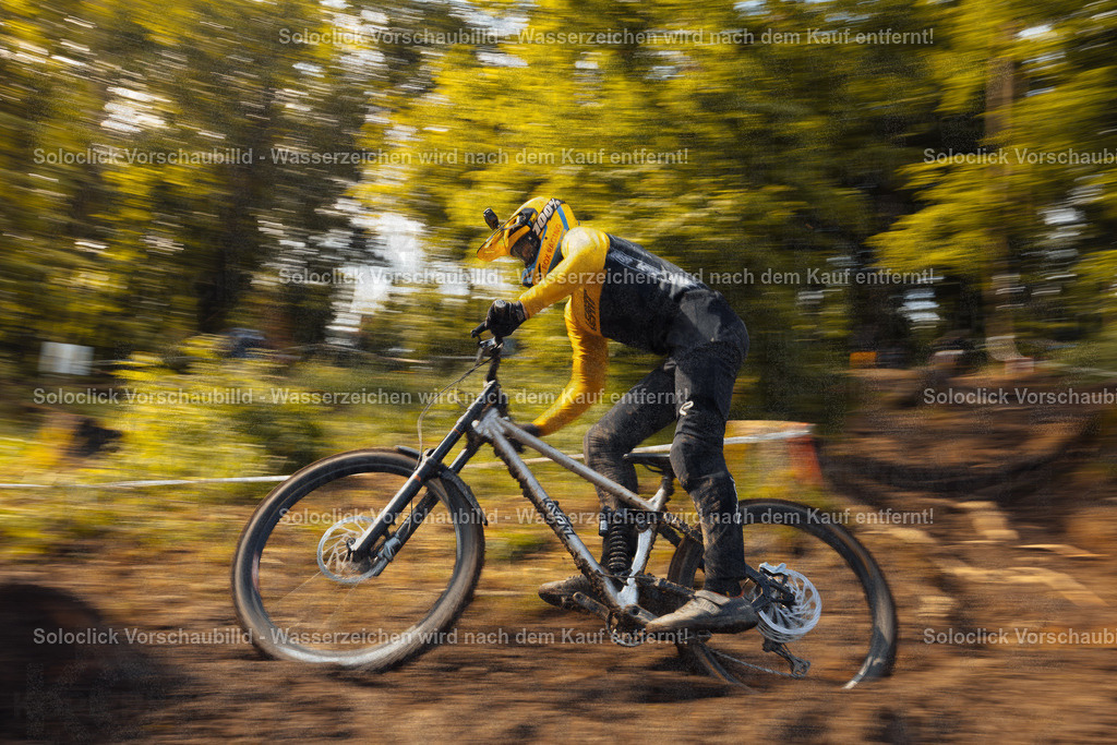 Dynamische Fahrt durch den Wald | Ein Mountainbiker in voller Ausrüstung rast auf einem staubigen, kurvigen Pfad durch einen dichten Wald. Die Bewegung des Fahrers und des Fahrrads ist durch die lange Belichtungszeit verschwommen, was die Geschwindigkeit und Dynamik der Szene betont. Der Fahrer trägt einen gelben Helm und eine gelbe Jacke, kombiniert mit schwarzen Hosen. Das Mountainbike ist ein Full-Suspension-Modell mit auffälligen Komponenten. - Realisiert mit Pictrs.com