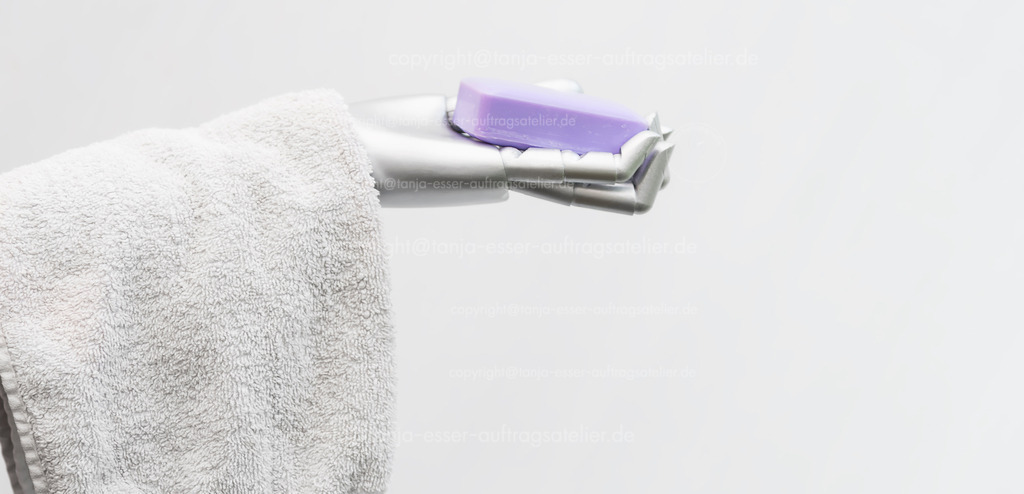 Robot takes care of people | Der Roboterarm hält Frotteehandtücher und ein Stück Seife in der Hand. Das Bild symbolisiert die Pflege von Menschen durch Maschinen. Konzeptuelles Foto vor weißem Hintergrund mit Copy Space