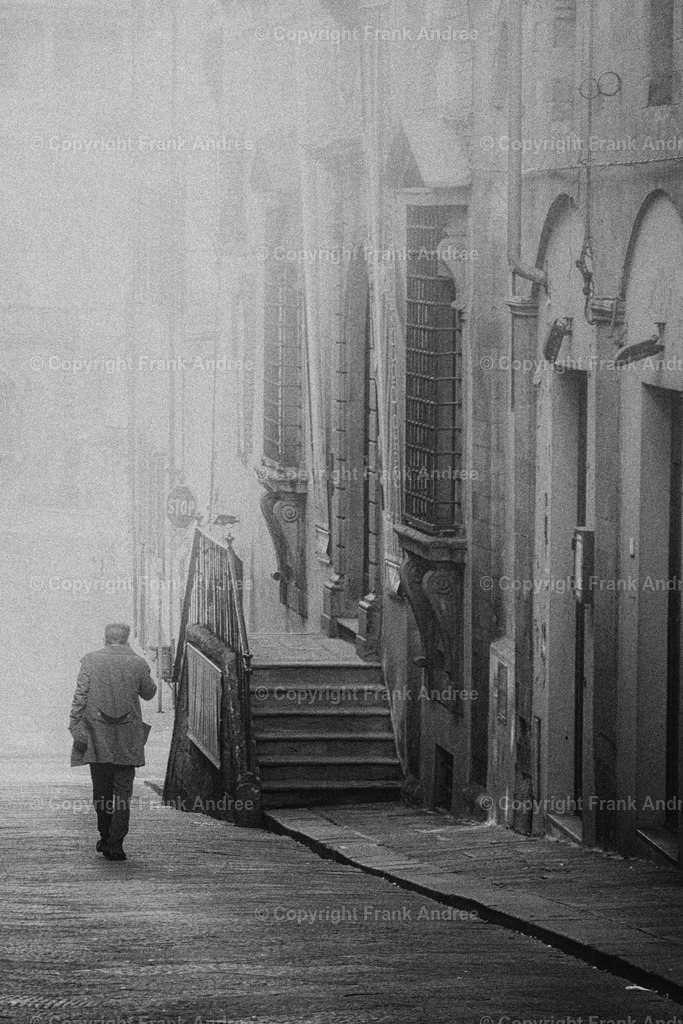 Pistoia | Ein Mann mit Mantel geht allein durch die bezaubernde Altstadt von Pistoia in der Toskana. Schwarz weiß street photography aus Italien. - Realisiert mit Pictrs.com