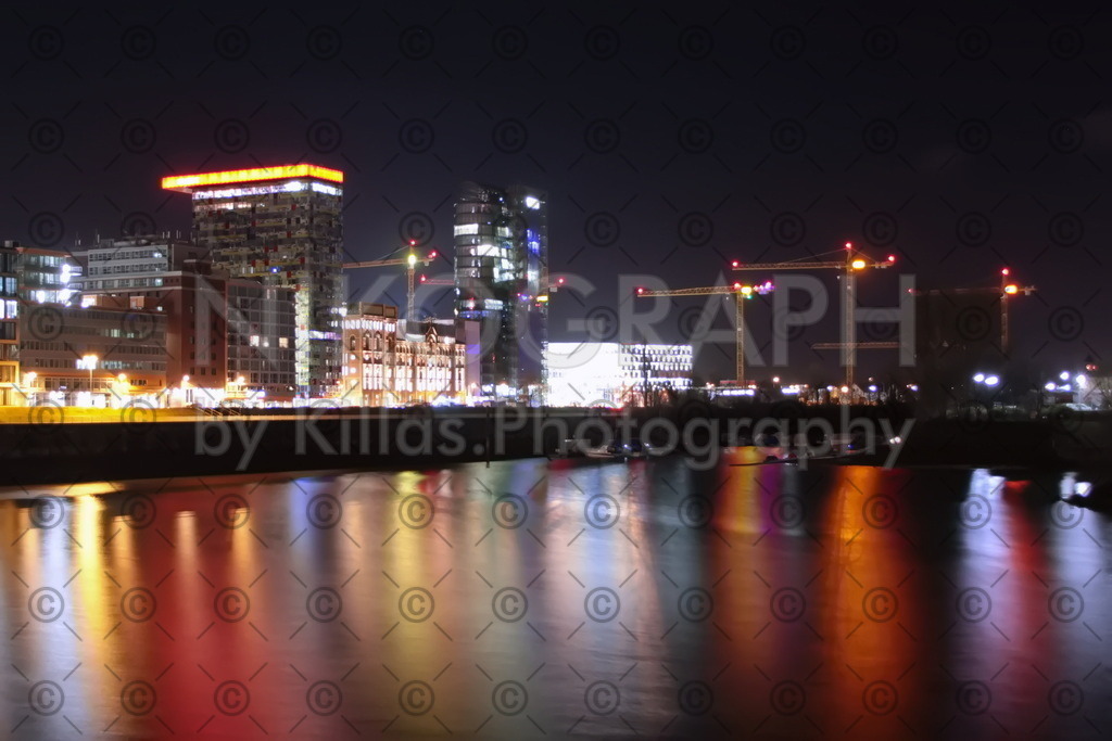 Düsseldorfer Hafen | Der Hafen von Düsseldorf bei Nacht. Die Lichter der Landeshauptstadt spiegeln sich im Wasser des Rheinhafens. Neben den Hochhäusern ragen Baukräne in den Nachthimmel.