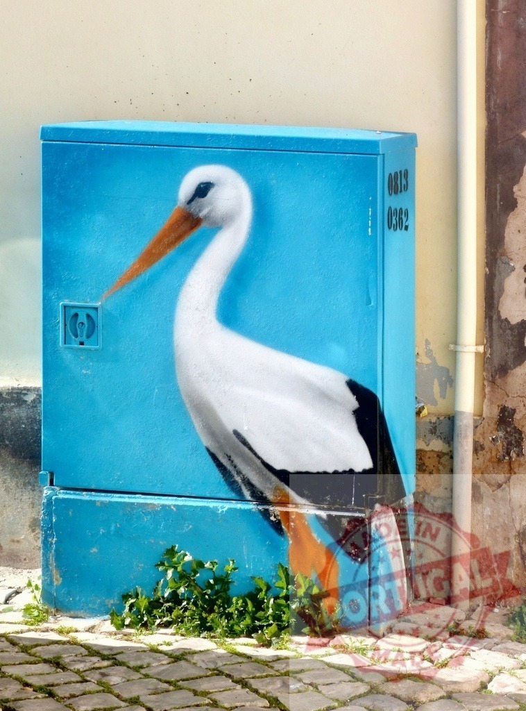 Stork street art painted on urban electrical box | Street art stork painted on an electrical box standing on cobblestone street - Realized with Pictrs.com