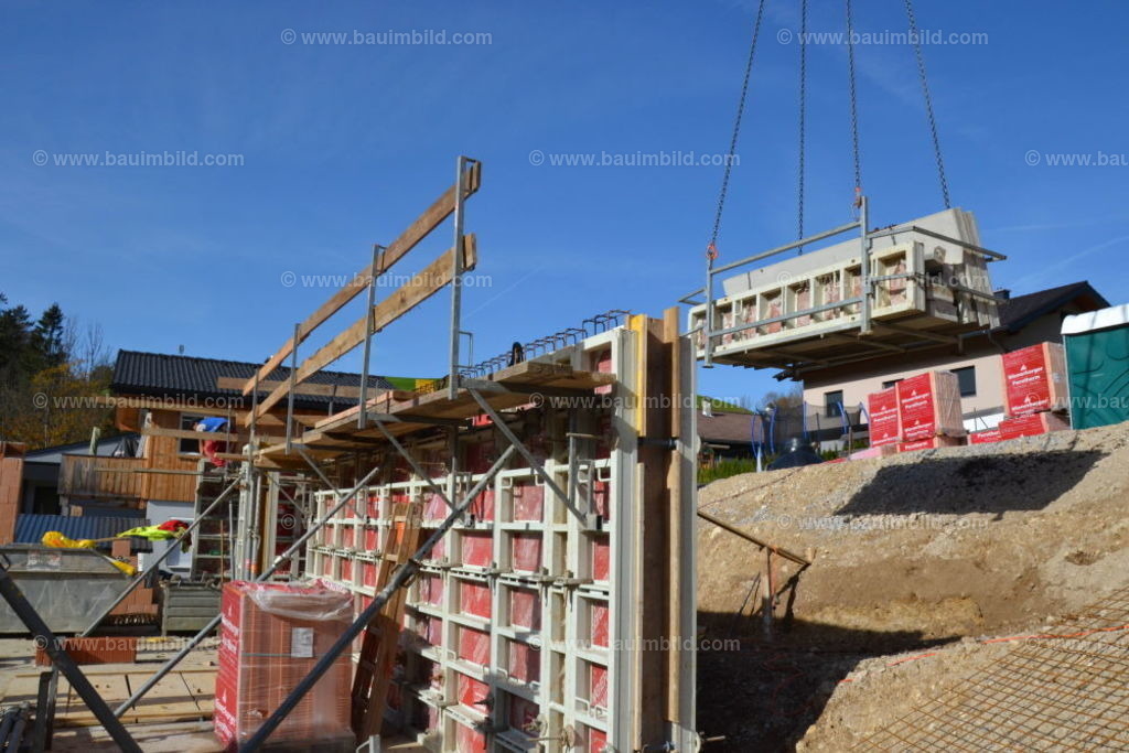 Schalung Betonwände mit Schutzgerüst | Fertig geschalte und bewehrte Betonwand mit Schutzgerüst für Betonierarbeiten, dahinter schwebende Kranlast aus Schalungsteilen, Hintergrund blauer Himmel