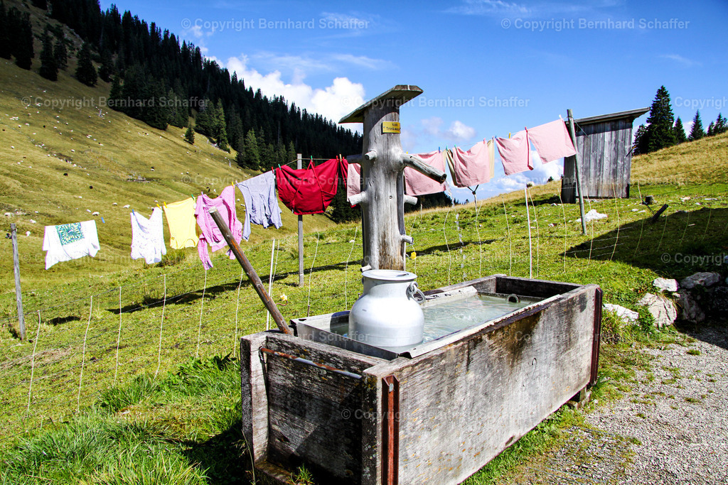 Wäsche an der Leine | Milchkanne in einem Wassertrog und gewaschene Wäsche an der Leine auf einer Almwiese. - Realisiert mit Pictrs.com