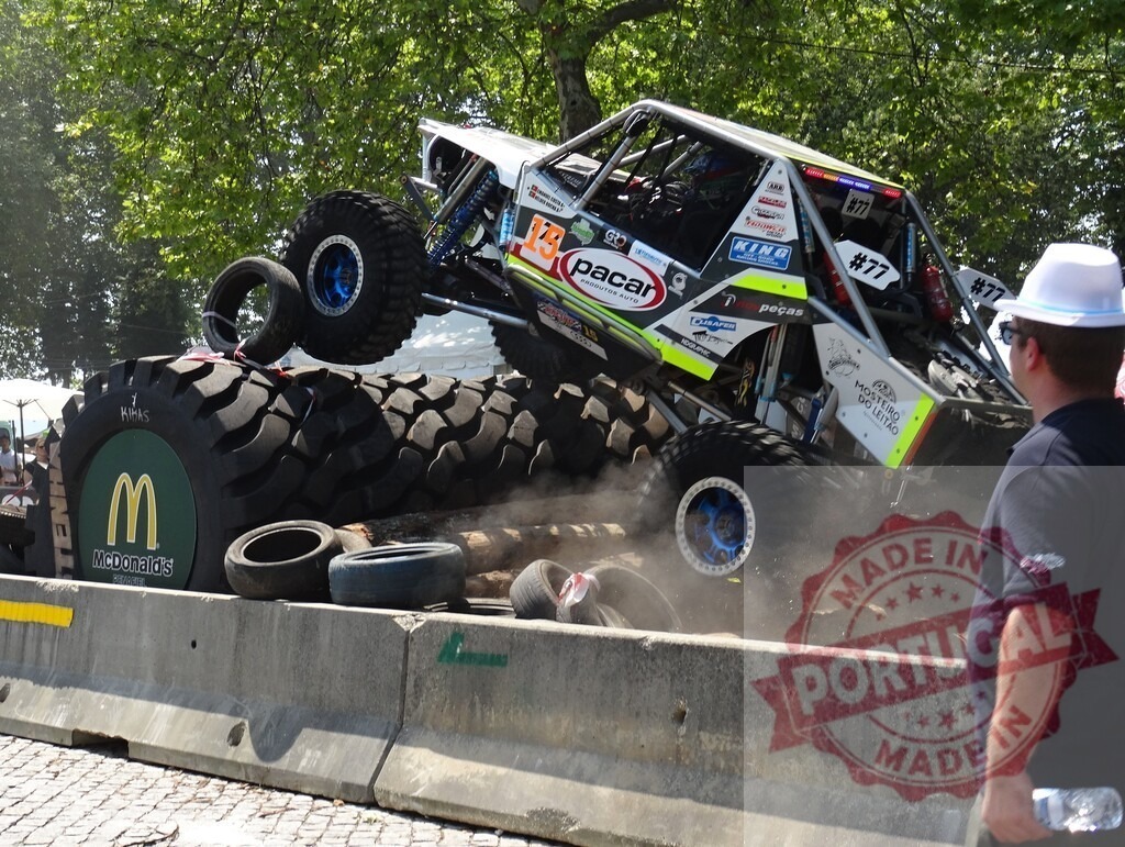 Four-wheel drive car climbing over tires during an off-road competition watched by a staff member | Powerful off-road vehicle overcoming obstacles during a challenging race, observed by a staff member - Realisiert mit Pictrs.com