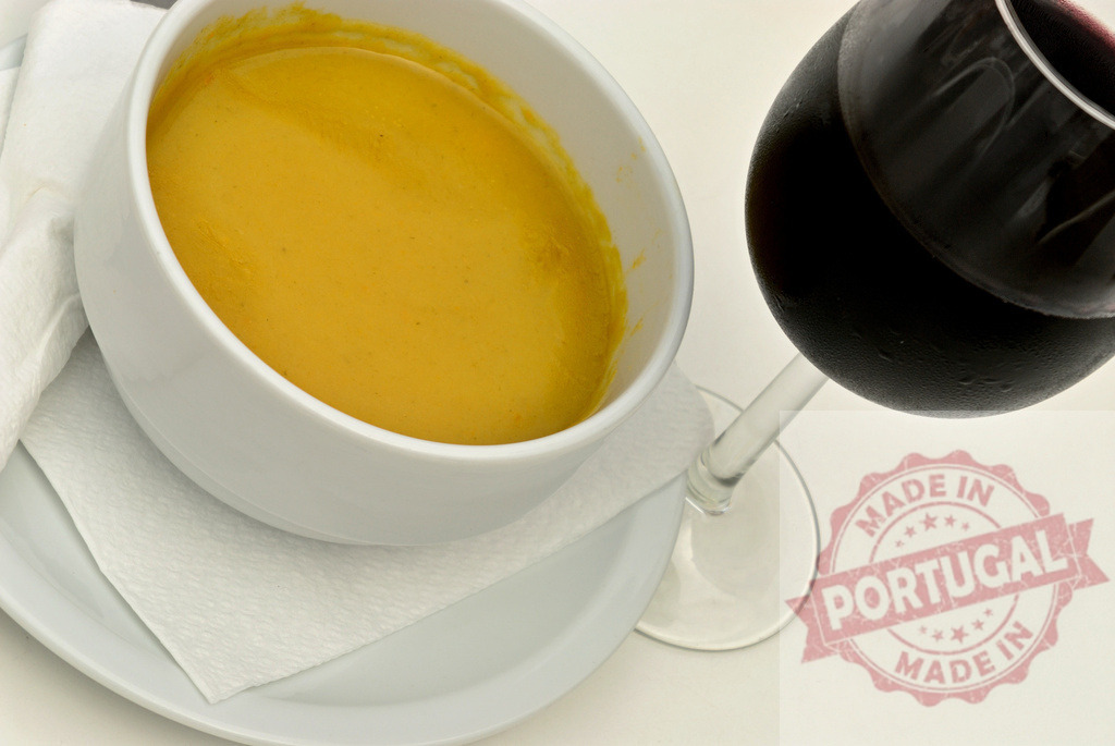 Creamy yellow soup and red wine glass dining | Creamy yellow soup in a white bowl served with a glass of red wine - Realized with Pictrs.com