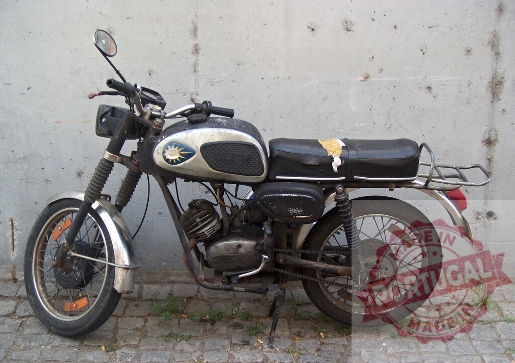 Old and rusty motorcycle parked against a concrete wall | Vintage motorcycle parked on a cobblestone street with a concrete wall in the background - Realisiert mit Pictrs.com