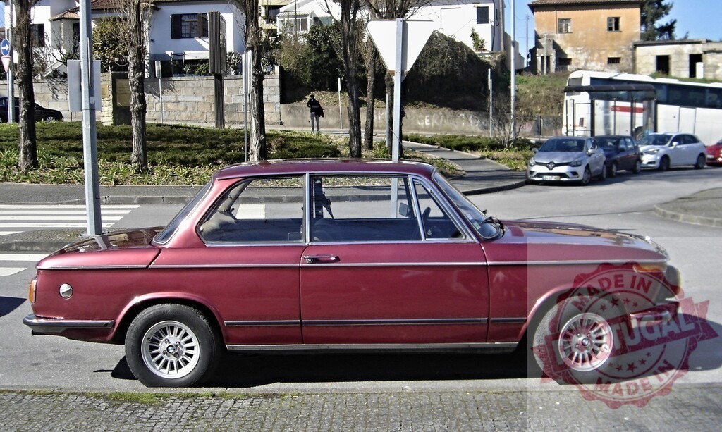 Classic BMW 2002tii parked on a street in Portugal | Shiny red BMW 2002tii parked on a residential street in Portugal, showcasing its timeless design - Realized with Pictrs.com