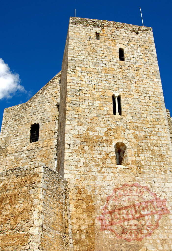 Ancient stone castle tower reaching blue sky. Provincia Castellon - Spain | Old stone castle tower standing tall against a bright blue sky with a white cloud - Realisiert mit Pictrs.com