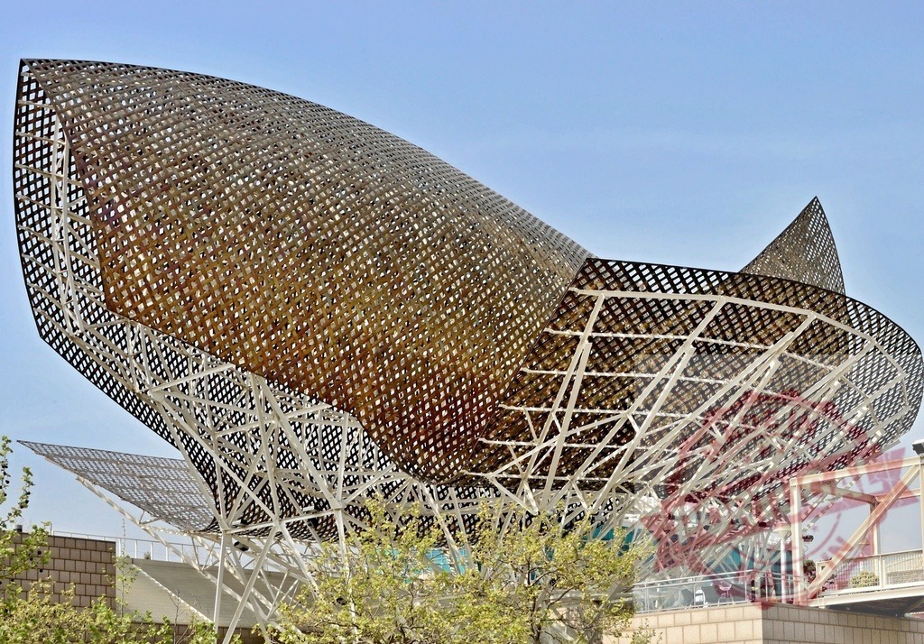 El Peix golden fish sculpture by Frank Gehry in Barcelona. Spain - Barcelona | El Peix, a large golden fish sculpture, standing against a clear blue sky in Vila Olímpica - Realisiert mit Pictrs.com