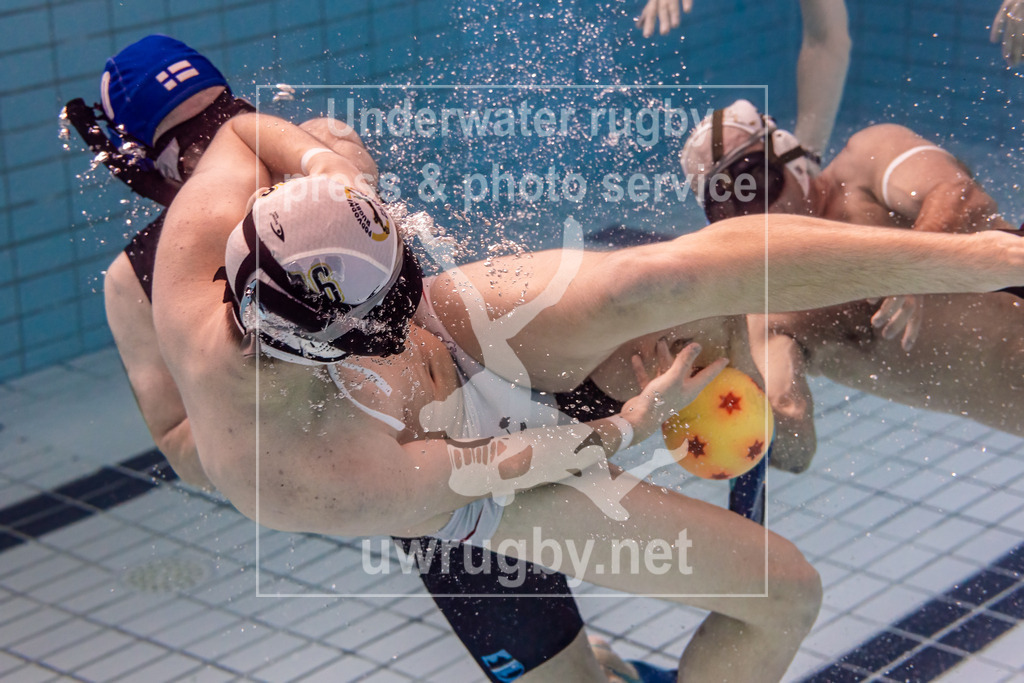 24. - 26.11.2023: Unterwasser-Rugby Champions Cup 2023  | HäSu (Hämeenlinna / Finnland) in blau gegen PF České Budějovice (Budweis / Tschechien) in weiß. Michael Honner (weiß #16) passt den Spielball zum Mitspieler, während er von einem finnischen Spieler angegriffen wird. - Realisiert mit Pictrs.com