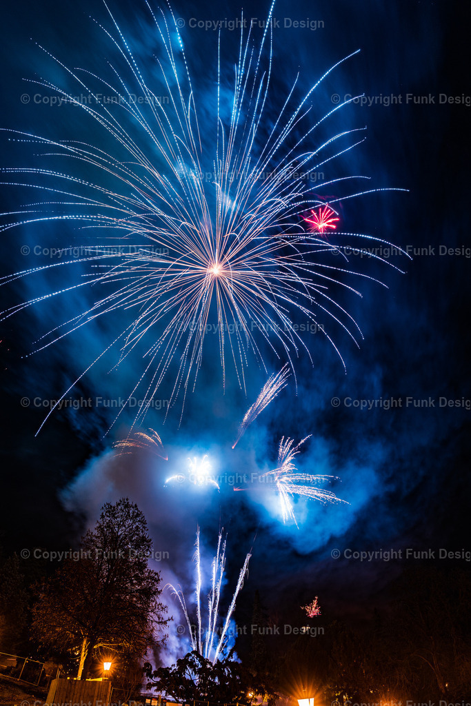 Silvester-Feuerwerk neben dem Casino Baden, Österreich | Blau-weißes Silvesterfeuerwerk erhellt den Nachthimmel mit kräftigen Explosionen, Rauch und sichtbaren Lichtspuren. Festliche Stimmung zum Jahreswechsel vor dunkler Baumkulisse.