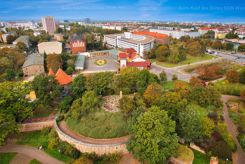 Magdeburg-Lukasklause-Denkmal-Otto-von-Guericke-5357 | Blick aus der Vogelperspektive auf die Lukasklause am Elbufer und das Hiroshima-Denkmal auf dem Lukashügel in Magdeburg. Zwei Orte, die auf den ersten Blick kaum miteinander verbunden wirken und doch beide von Krieg, Zerstörung und dem Wunsch nach Frieden erzählen.Die Lukasklause geht auf einen mittelalterlichen Wehrturm zurück, der bereits im 13. Jahrhundert Teil der Magdeburger Stadtbefestigung war. 1631 lag die Anlage während der Zerstörung Magdeburgs im Mittelpunkt der Kämpfe. Heute befindet sich hier das Otto-von-Guericke-Zentrum.Nur wenige Meter entfernt erinnert die Stele der Völkerfreundschaft an die Atombombenabwürfe auf Hiroshima und Nagasaki im August 1945. Unter einer Glasplatte befindet sich ein Stein aus Nagasaki, der aus der 1945 zerstörten Stadt nach Magdeburg gebracht wurde. Die Inschrift „Hiroshima und Nagasaki mahnen“ macht den Ort zu einer Gedenkstätte für Frieden und Völkerverständigung. So liegen auf engem Raum fast 800 Jahre Magdeburger Geschichte nebeneinander – vom mittelalterlichen Wehrturm bis zur Mahnung an die Schrecken des modernen Krieges. - Realisiert mit Pictrs.com