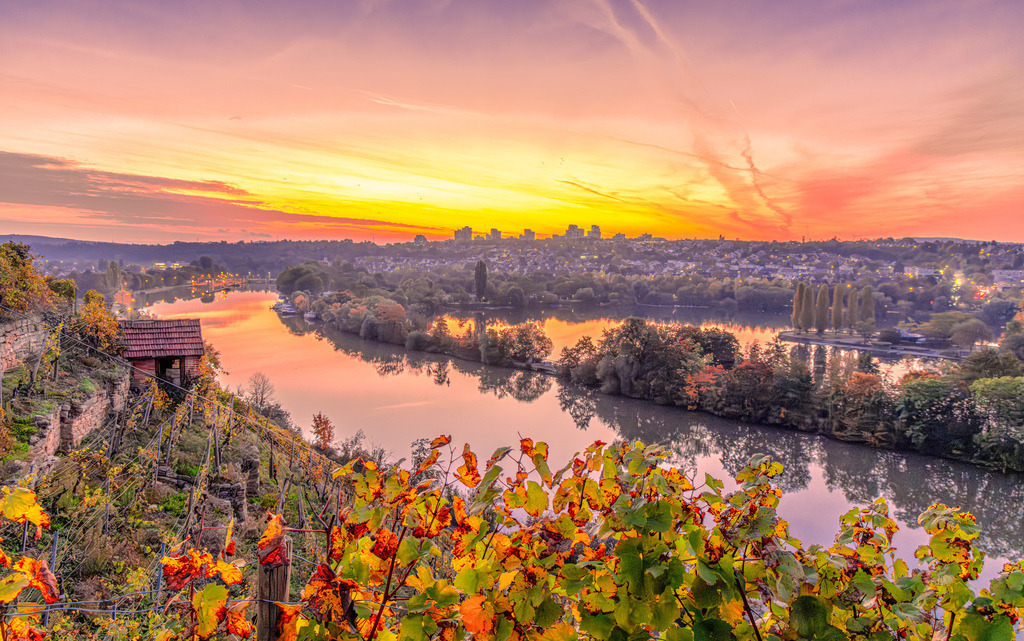 Malerischer herbstlicher Blick auf den Neckar und die Weinberge bei Sonnenaufgang,Stuttgart-Hofen | Das Bild zeigt einen malerischen Blick auf den Neckar und die Weinberge bei Stuttgart-Hofen in der Nähe des Max-Eyth-Sees im Morgenlicht.Ort: Stuttgart (Hofen / Blick vom Weinberg auf den Neckar)Landschaft: Weinberge im Vordergrund mit herbstlich oder abendlich gefärbten Blättern, der gewundene Flusslauf des Neckars und ein weicher, farbintensiver Sonnenauf- oder -untergang.Besonderheit: Ein kleines Weinberg-Häuschen am steilen Hang links - Realisiert mit Pictrs.com