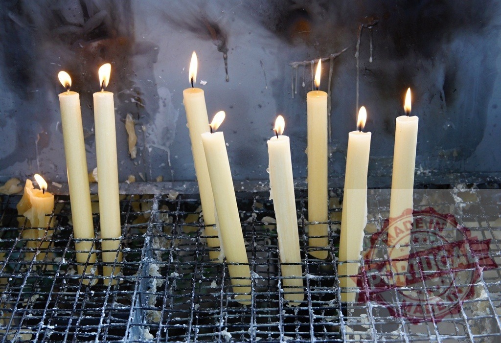 Burning candles illuminating dark sacred temple space | Burning candles creating a spiritual atmosphere on a metal grate, with melting wax and soot - Realisiert mit Pictrs.com