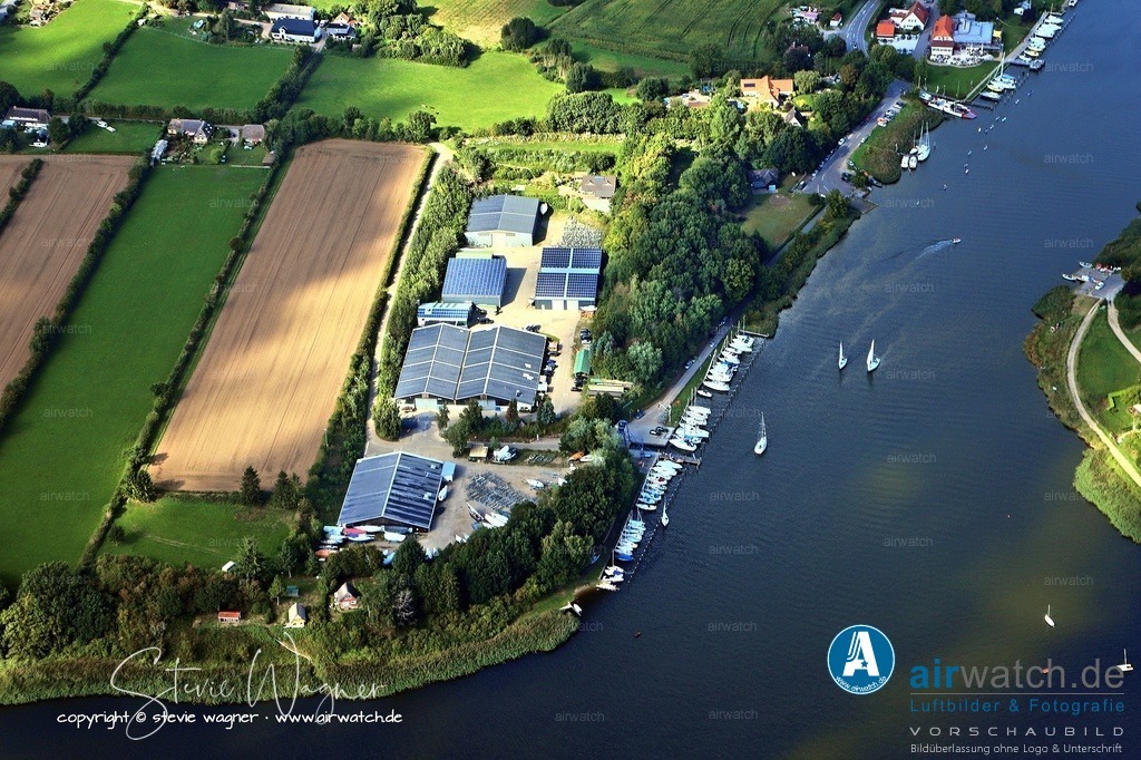 Luftbild Ostseefjord Schlei, Missunde, Campingplatz Wees, Fährhaus Missunde, Marina Brodersby | Missunde ist ein Dorf an der engsten Stelle der Schlei in Schleswig-Holstein, Deutschland, und gehört zur Gemeinde Kosel. Der Ort ist historisch bedeutend, da er seit dem 12. Jahrhundert aufgrund seiner strategischen Lage an der Schlei wiederholt umkämpft war. - Heute verbindet die Schleifähre Missunde die beiden Ufer der Schlei zwischen Missunde (Schwansen) und Brodersby (Angeln). Die aktuelle Fähre, Missunde II, wurde 2003 eingeführt und verkehrt ganzjährig, wochentags von 6 bis 22 Uhr und am Wochenende von 8 bis 22 Uhr. Sie kann bis zu 45 Personen sowie Fahrzeuge transportieren. Die Fähre ist ein beliebtes Erlebnis für Touristen und Einheimische.