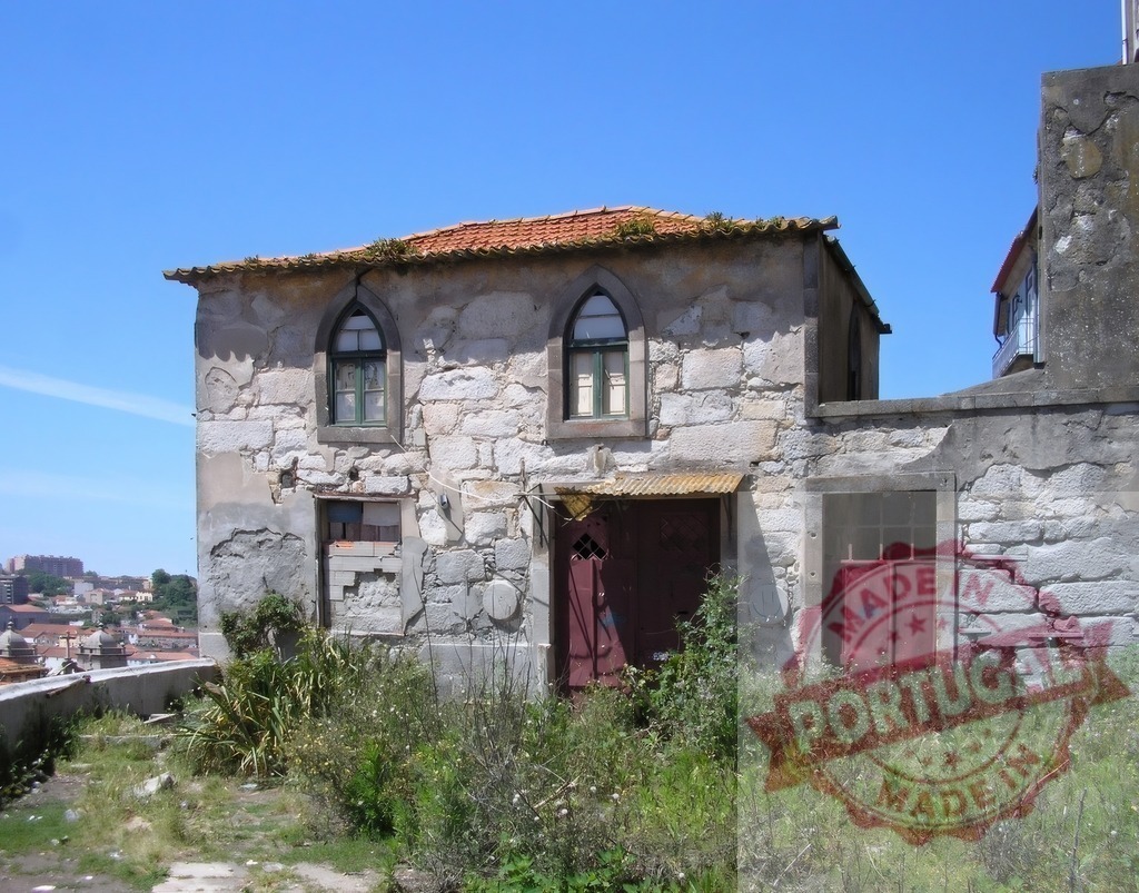 Old stone house with boarded windows in Porto, Portugal | Dilapidated stone house standing abandoned with overgrown weeds and a clear blue sky - Realized with Pictrs.com