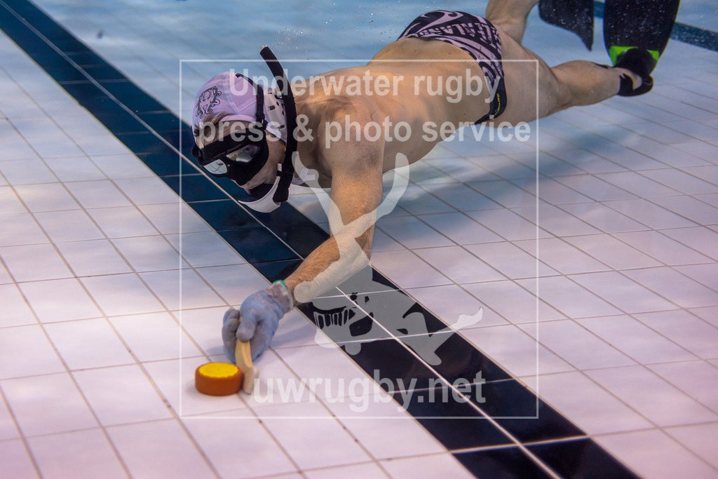 Unterwasser-Hockey: Rückrunde Liga 2023/2024 - Bild 19 | Spieler mit weißer Spielkappe und weißen Stick spielt den Puck entlang des Bodes des Schwimmbeckens. - Realisiert mit Pictrs.com
