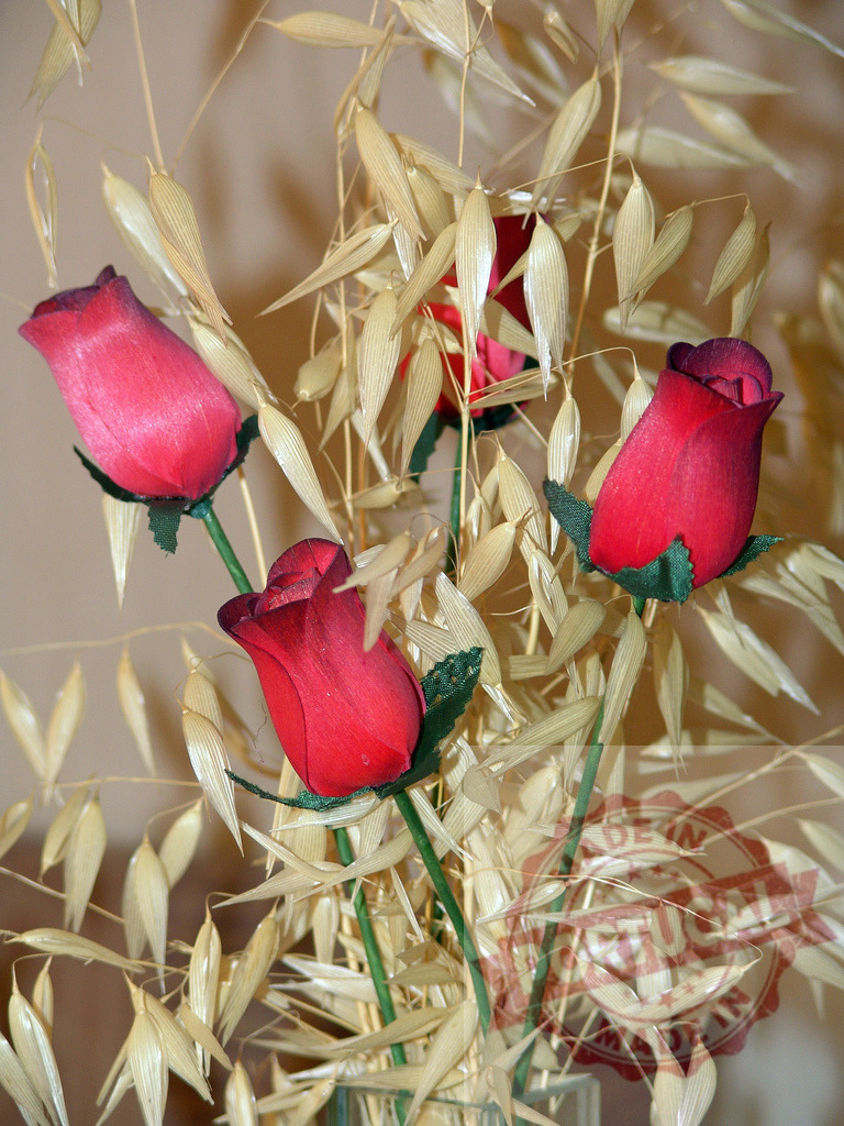 Red wooden roses standing among dry oat stalks | Decorative composition of red wooden roses and dry oat stalks creating a rustic and romantic atmosphere - Realized with Pictrs.com