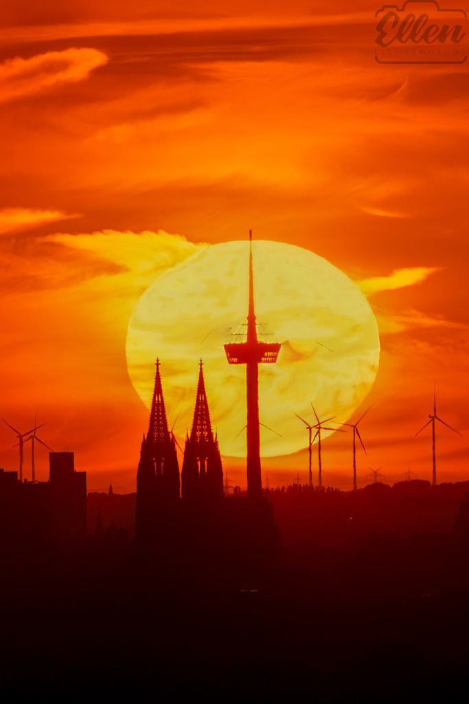 Sun Aligned | Perfectly aligned with the setting sun, Cologne’s skyline transforms into a silhouette of light and geometry. The cathedral spires and the Colonius Tower rise against the glowing orb — a fleeting alignment between architecture and nature. - Realisiert mit Pictrs.com