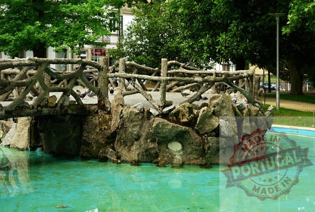 Concrete footbridge with pigeons over a green pond in park. Portugal - Norte | Concrete bridge with a faux wood design spanning a park pond with pigeons resting on it - Realized with Pictrs.com