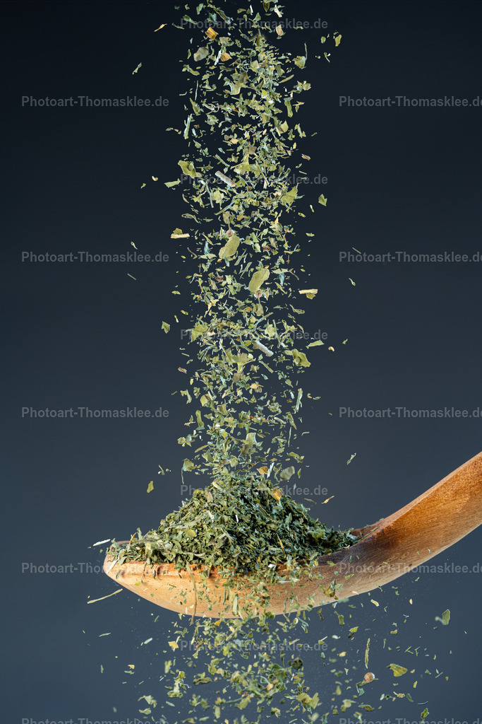 Getrocknete Basilikumblätter – Intensives Aroma für mediterrane Genüsse | Getrocknete Basilikumblätter – Intensives Aroma für mediterrane Genüsse. Kollektion: A spoon of tastefully seasonings.In einer kraftvollen Momentaufnahme fallen getrocknete Basilikumblätter auf einen rustikalen Holzlöffel und schweben scheinbar schwerelos vor einem sanft verlaufenden, dunklen blaugrauen Hintergrund. Die Highspeed-Fotografie friert die Bewegung perfekt ein und hebt die feine Struktur und intensive grüne Farbe der Blätter hervor. Dieses Bild verbindet Natürlichkeit mit Dynamik und eignet sich ideal für Themen rund um gesunde Ernährung, mediterrane Küche, frische Zutaten und kreative Food-Inszenierungen. Die harmonische Farbgestaltung unterstützt die moderne, ruhige Atmosphäre.Das Bild könnte sehr gut in folgenden Räumen gut platziert werden:Esszimmer – als stilvolle Wanddekoration rund um das Thema gesunde und natürliche Küche.Küche – als inspirierendes Motiv für Kochbegeisterte und Liebhaber mediterraner Aromen.Café oder Bistro – im Gästebereich zur Betonung einer frischen, naturnahen Küche und eines modernen Ambientes. - Realisiert mit Pictrs.com