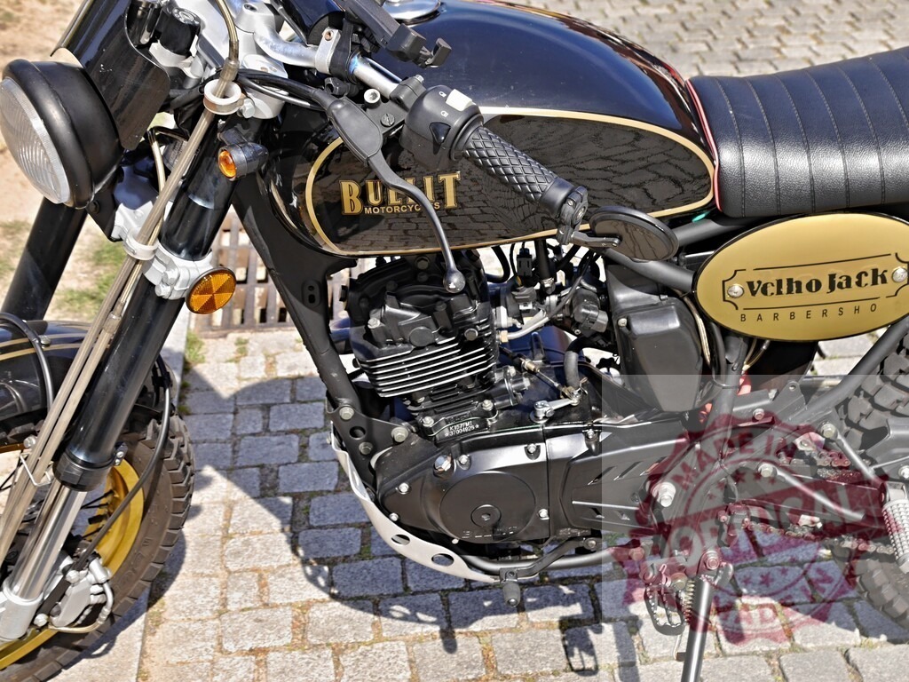 Bullit Motorcycle parked on cobblestone street, showcasing engine details and barbershop branding | Close-up of a Bullit Motorcycle parked on a cobblestone street, highlighting its engine, design, and Velho Jack Barbershop branding - Realized with Pictrs.com