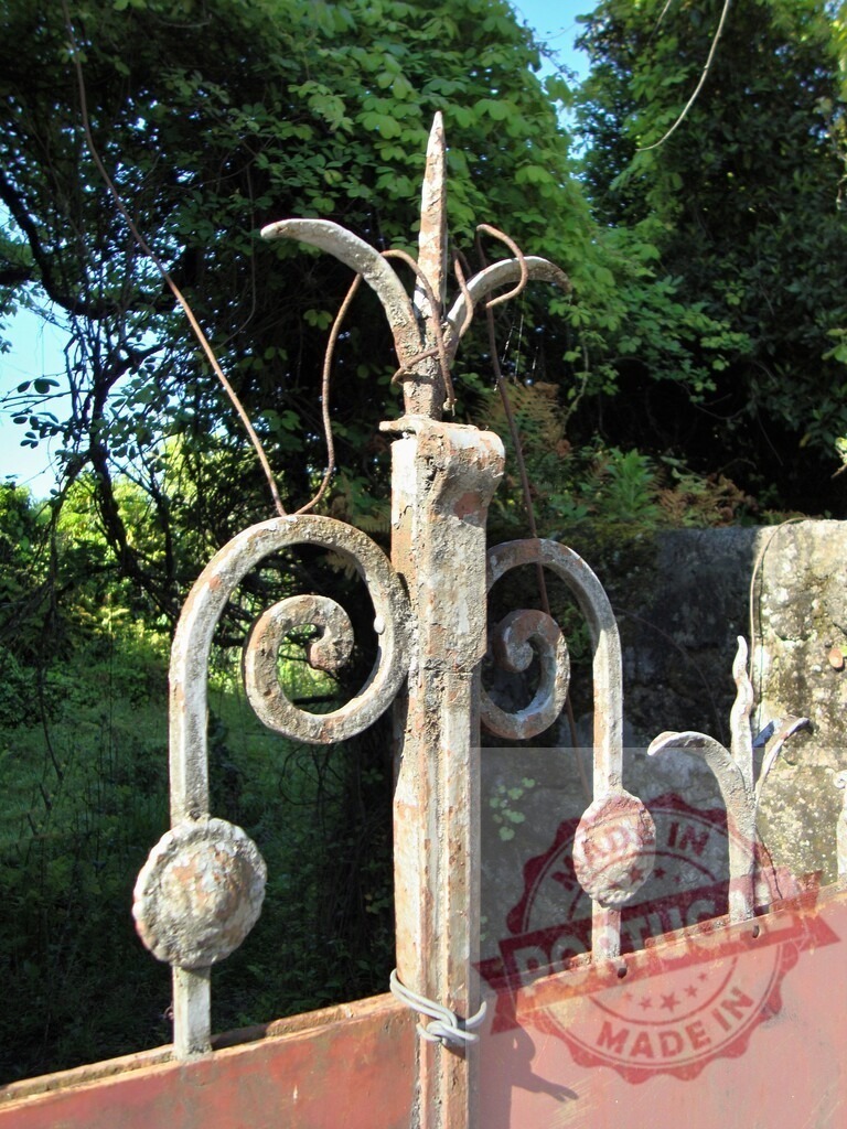 Old rusty wrought iron gate finial detail | Weathered ornate metal gate top with decorative finial against green foliage - Realisiert mit Pictrs.com