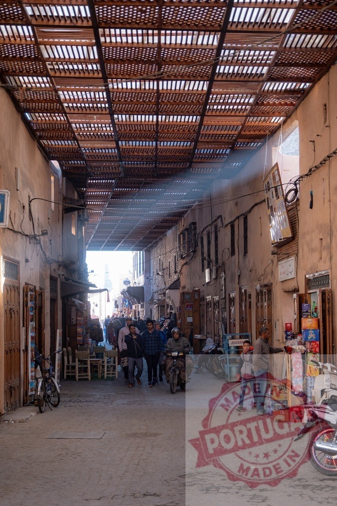 People walking in a covered street market in Morocco | Tourists and locals walking in a narrow covered street in a Moroccan market, surrounded by shops and stalls - Realized with Pictrs.com