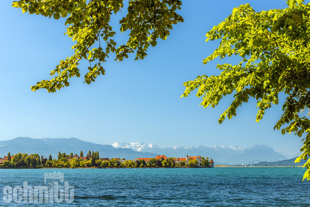 Idyllischer Blick auf die Insel Lindau mit Bergpanorama | Die Insel Lindau präsentiert sich inmitten des Bodensees vor einer beeindruckenden Bergkulisse. Der idyllische Blick über das ruhige Wasser und die dahinterliegenden Alpen verbindet die besondere Atmosphäre der Insel mit der Weite der Landschaft. - Realisiert mit Pictrs.com