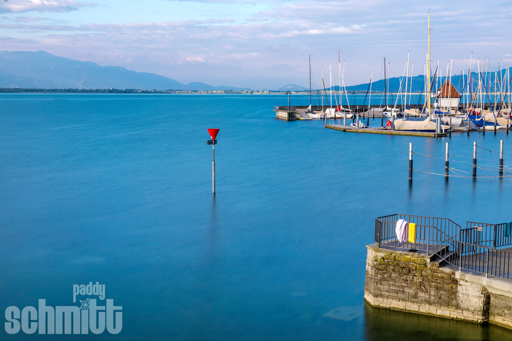 Langzeitbelichtung am Lindauer Hafen am Bodensee | Eine Langzeitbelichtung am Lindauer Hafen verwandelt den Bodensee in eine ruhige, fast zeitlose Szenerie. Das sanft geglättete Wasser und die Lichter des Hafens verleihen der Aufnahme eine besondere Tiefe und eine stimmungsvolle Atmosphäre. - Realisiert mit Pictrs.com