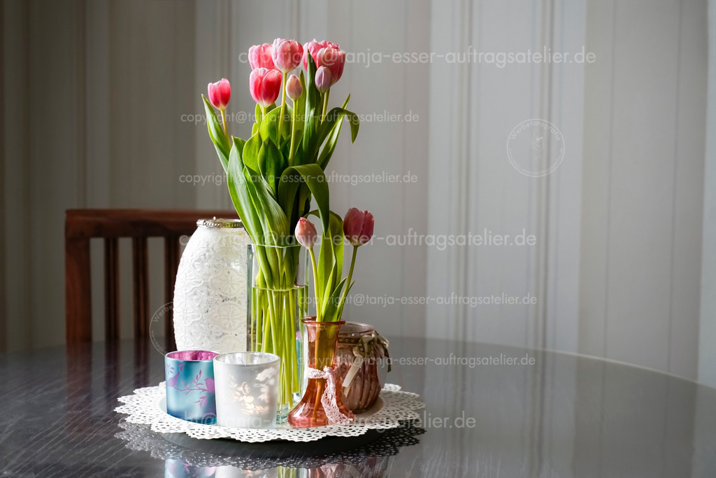 Rosa Tulpen auf Tisch D | Langstielige pinke Tulpen mit mehreren Glasgefäßen auf einem runden Holztisch. Im Hintergrund ist ein Stuhl und gestreifte Tapete. Antiker romantischer Look.                               