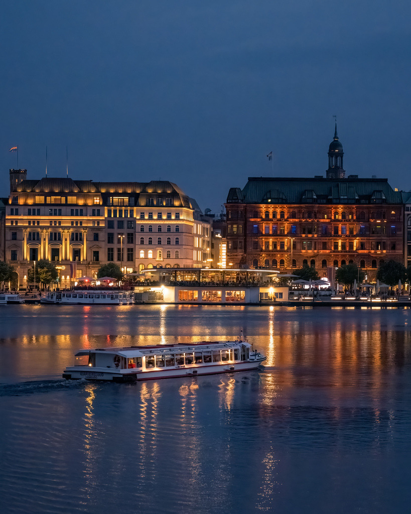 Lichter der Hamburger Binnenalster | Die beleuchteten Fassaden der Hamburger Innenstadt spiegeln sich am Abend im Wasser der Binnenalster. Die warme Architekturbeleuchtung bildet einen eindrucksvollen Kontrast zum tiefblauen Himmel. - Realisiert mit Pictrs.com