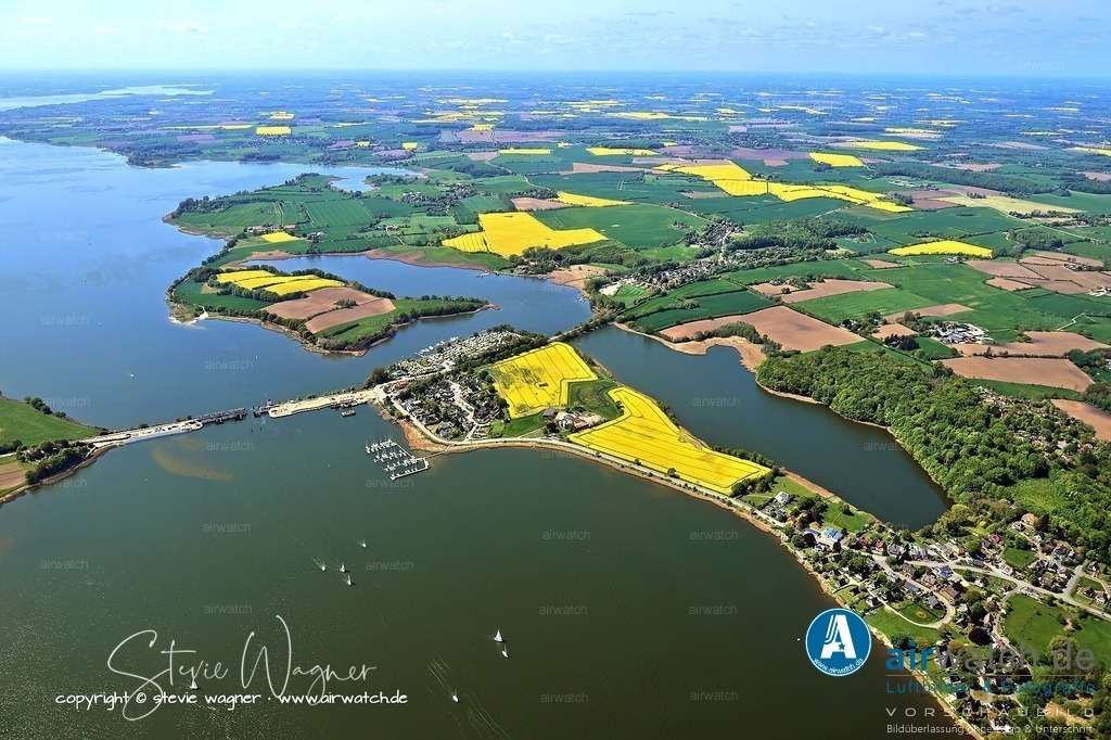 Luftbild Ostseefjord Schlei, Boren-Lindaunis Schleibrücke, Campingplatz Lindaunis, Sportboothafen Lindaunis | Schleibrücke Lindaunis - Die Kosten für den Neubau stiegen von ursprünglich 46 Millionen Euro auf über 84 Millionen Euro. Die neue Brücke soll 126 Meter lang sein, die Straße von einem auf zwei Fahrstreifen verbreitert werden, und Fußgänger sowie Radfahrer sollen erstmals einen drei Meter breiten Weg erhalten. Die alte Brücke wird abgebaut und durch den Neubau ersetzt.